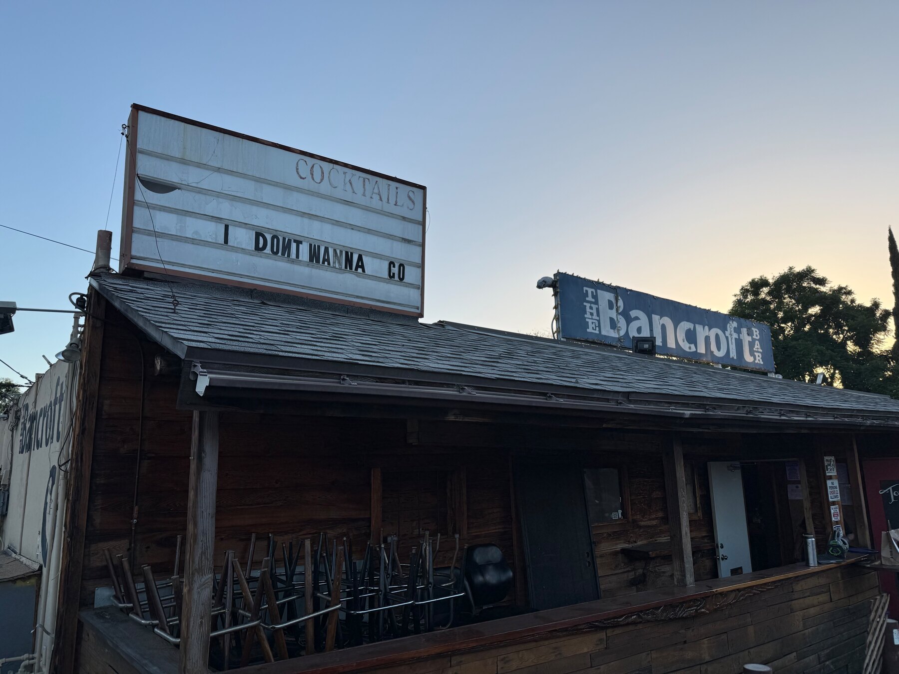 The Bancroft Bar at dusk. The marquee reads I DONT WANNA GO and the bar stools are stacked on the patio.